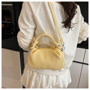 Detail view of yellow pleated handbag with ring handle and detachable shoulder strap