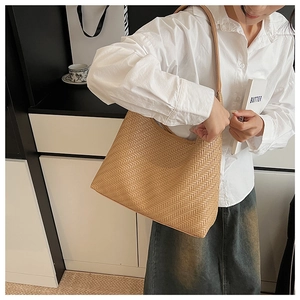 Detail of a large brown woven tote bag with herringbone texture and slim shoulder strap