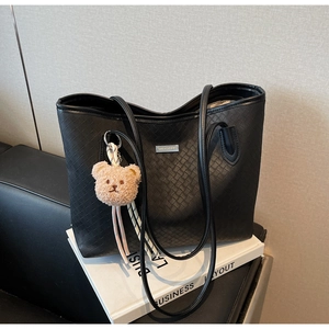 Detail view of black woven leather tote bag featuring a metal logo and plush bear charm