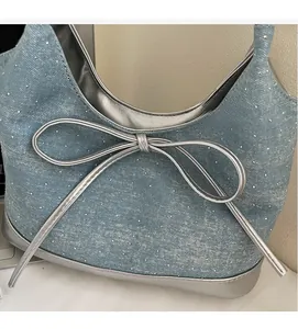 Detail of light blue denim tote bag with silver bow ornament and metallic trim