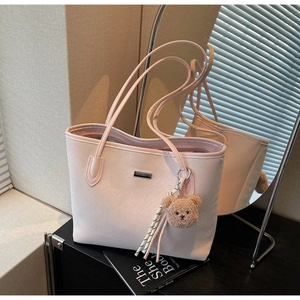 Detail of light pink tote bag with woven texture, metal logo and plush bear charm