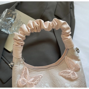 Detail of pink dumpling bag featuring 3D butterfly embroidery and a ruched handle