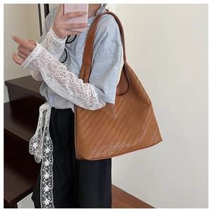 Detail showing the brown woven leather texture and shoulder strap of a tote bag
