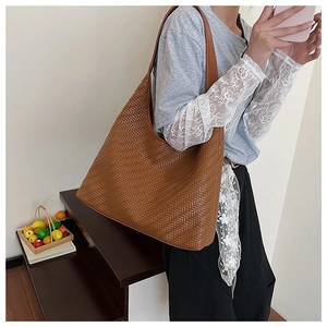 Detail of a brown woven tote bag featuring an intricate pattern and a wide shoulder strap