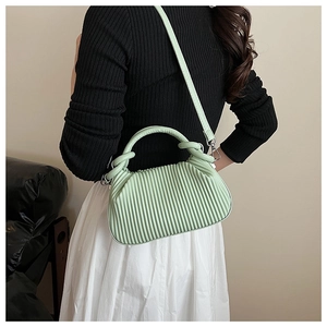 Detail of mint green pleated handbag with knot handle worn by a model on shoulder
