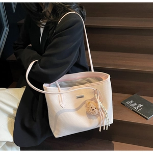 Detail view of pink woven tote bag featuring metal logo plate and plush bear charm