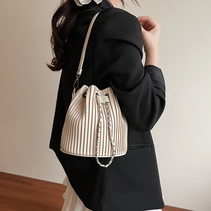 Beige pleated bucket bag with chain drawstring and shoulder strap worn by model