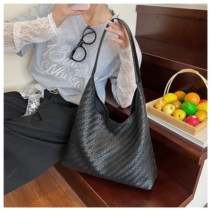 Detailed close-up of the black woven leather tote bag texture and large shoulder strap