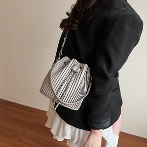 Light grey pleated drawstring bucket bag with silver chain strap worn by a female model