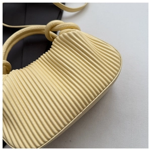 Detail of cream pleated handbag featuring cylinder handle and intricate knot design