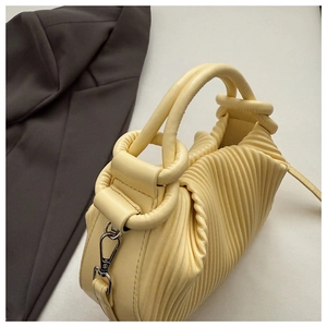 Detail of creamy yellow pleated handbag with wavy texture and round tube handle