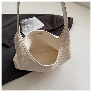 Macro detail of creamy white shoulder bag showing V-shaped woven texture and magnetic buckle