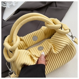 Macro detail of yellow pleated handbag showing ring handle and metallic magnet closure