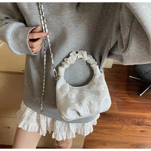 Detail of white butterfly lace crossbody bag featuring a ruched handle and silver chain