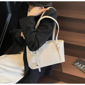 Detailansicht der cremefarbenen Tasche mit Perlenanhänger und glänzendem Finish