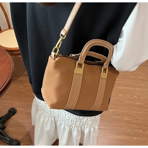 Model wearing a camel Boston tote bag with adjustable strap in a warm interior setting