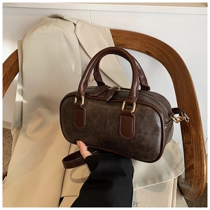 Detailed close-up of dark brown vintage Boston bag with brushed gold hardware on wooden chair