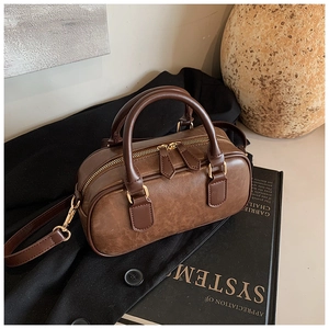 Detailed top view of retro brown Boston bag with golden zippers on black blazer and books
