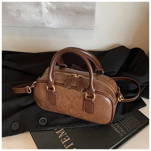 Detail of a dark brown cylindrical Boston bag with retro leather texture and gold zippers