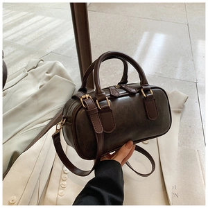 Detail of a dark brown vintage Boston handbag with golden hardware on a white blazer