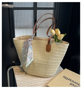 Detail of straw woven tote bag with brown leather handles and decorative silk scarf