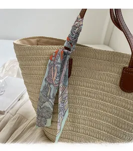 Detail of woven straw tote bag with green printed silk scarf and leather handle