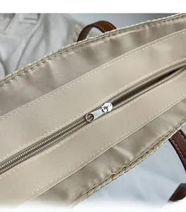 Detail of silver zipper closure and brown leather handle on woven straw bucket bag