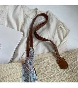 Detail of woven straw tote bag featuring brown leather straps and blue floral silk scarf