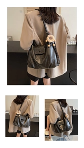 Detail of black matte tote with lion plush charm and woven shoulder strap on female model