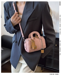 Close-up of pink Boston bag with brown leather handles and silver rivet details