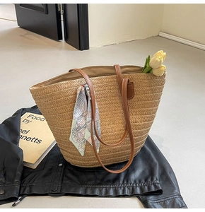 Detail of woven straw tote bag featuring brown leather handles and a printed silk scarf