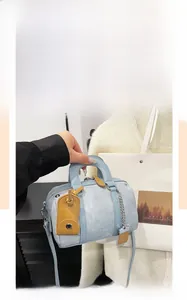 Detail of light blue Boston handbag featuring yellow leather tag and silver chain