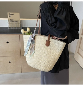 Detail of woven straw tote bag with brown leather straps and vintage print silk scarf