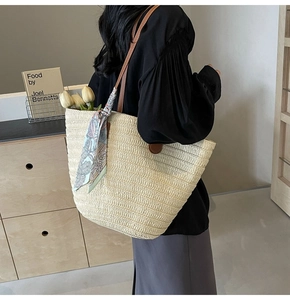 Detail of hand-woven straw tote with leather strap and decorative floral scarf on shoulder