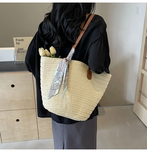 Detail of straw tote bag with brown leather handles and decorative floral silk scarf