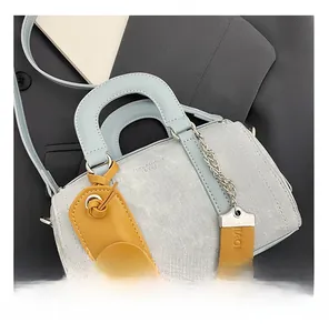 Detailed macro view of light blue denim Boston bag with tan leather charm on grey suit