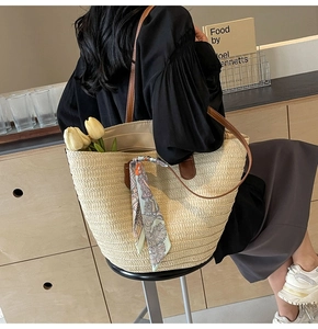 Detail view of the hand-woven straw tote bag with brown leather handles and silk scarf decoration