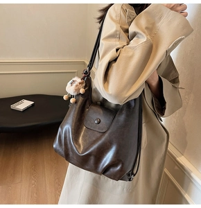 Detail of vintage brown leather tote bag with a small lamb pendant on a model's shoulder