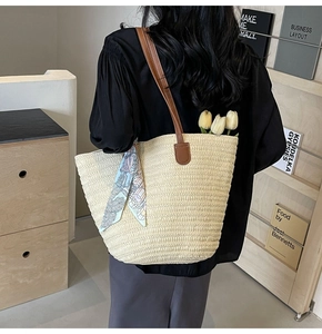 Detail of woven straw tote bag featuring leather handles and decorative floral silk scarf