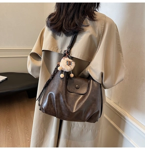 Detail of dark brown leather tote bag with plush lion charm and woven strap accents