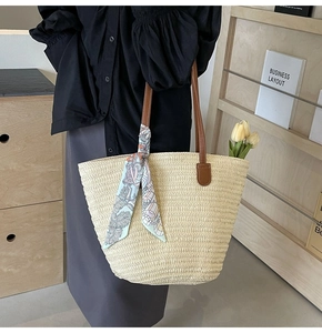 Detail of woven straw tote bag with brown leather handles and a decorative silk scarf