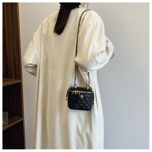 Detailed back view of a black quilted bucket bag with gold chain strap on a cream coat