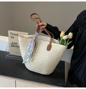 Detail of straw woven tote bag with brown leather handles and a blue patterned silk scarf