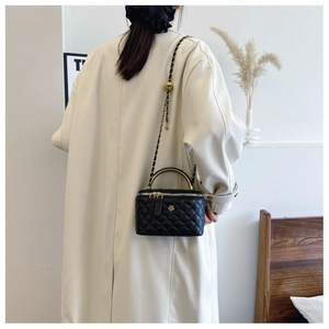 Detail of black quilted bucket bag with gold chain strap and floral metal clasp
