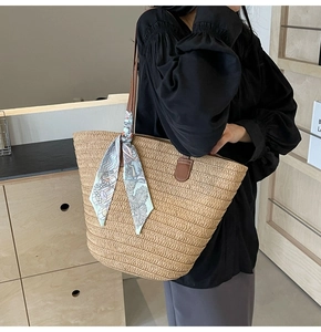 Detail of straw tote bag with printed silk scarf handle and leather strap on shoulder