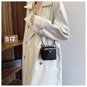 Detail of a black quilted leather bucket bag with gold chain strap worn by a model
