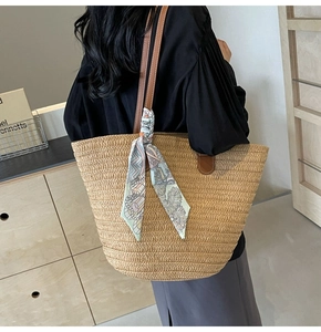 Detail of straw tote bag with brown leather handles and decorative geometric scarf