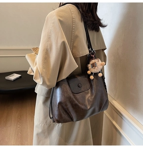 Detail of dark brown leather tote bag with vintage texture and plush alpaca charm