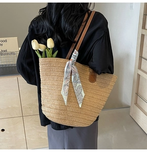 Detail of straw woven tote bag with brown leather strap and floral scarf decoration