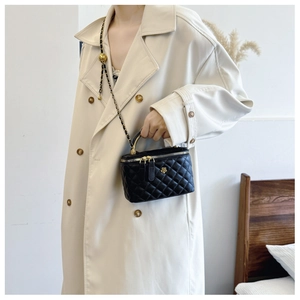 Detail of black quilted bucket bag featuring a gold chain strap and metal handle